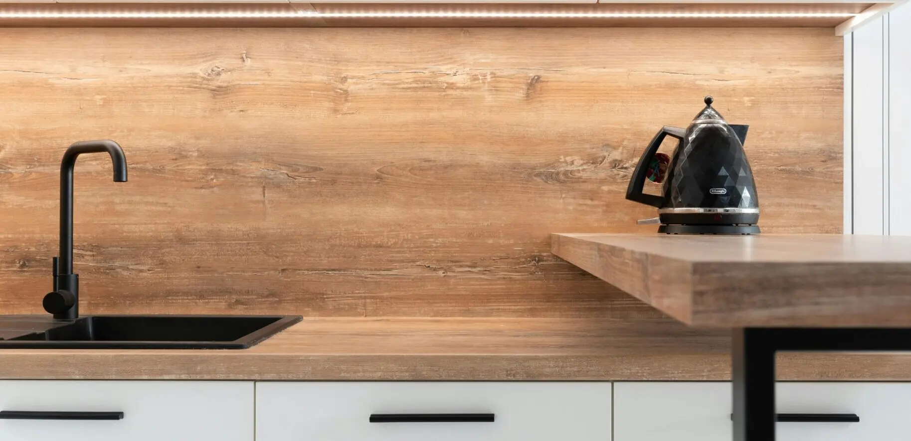 A sleek modern kitchen with wooden backsplash and black kettle, highlighting minimalist design.